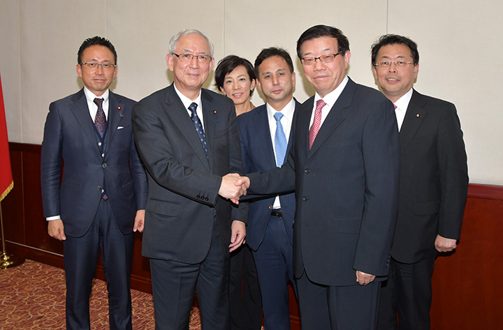 李主任（右から2人目）と握手する井上幹事長（左隣）ら公明党のメンバー＝27日　北京市
